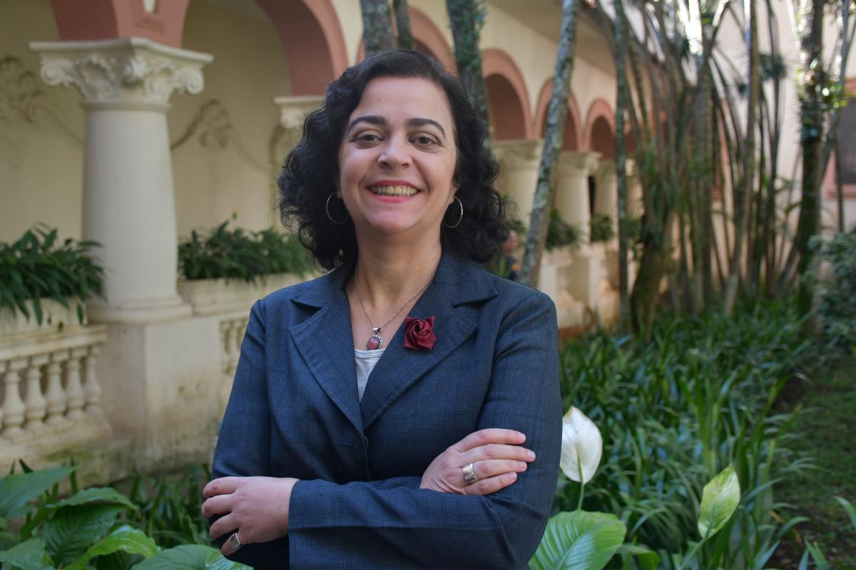 Mulher de cabelos pretos cacheados e roupa azul, em frente a um jardim